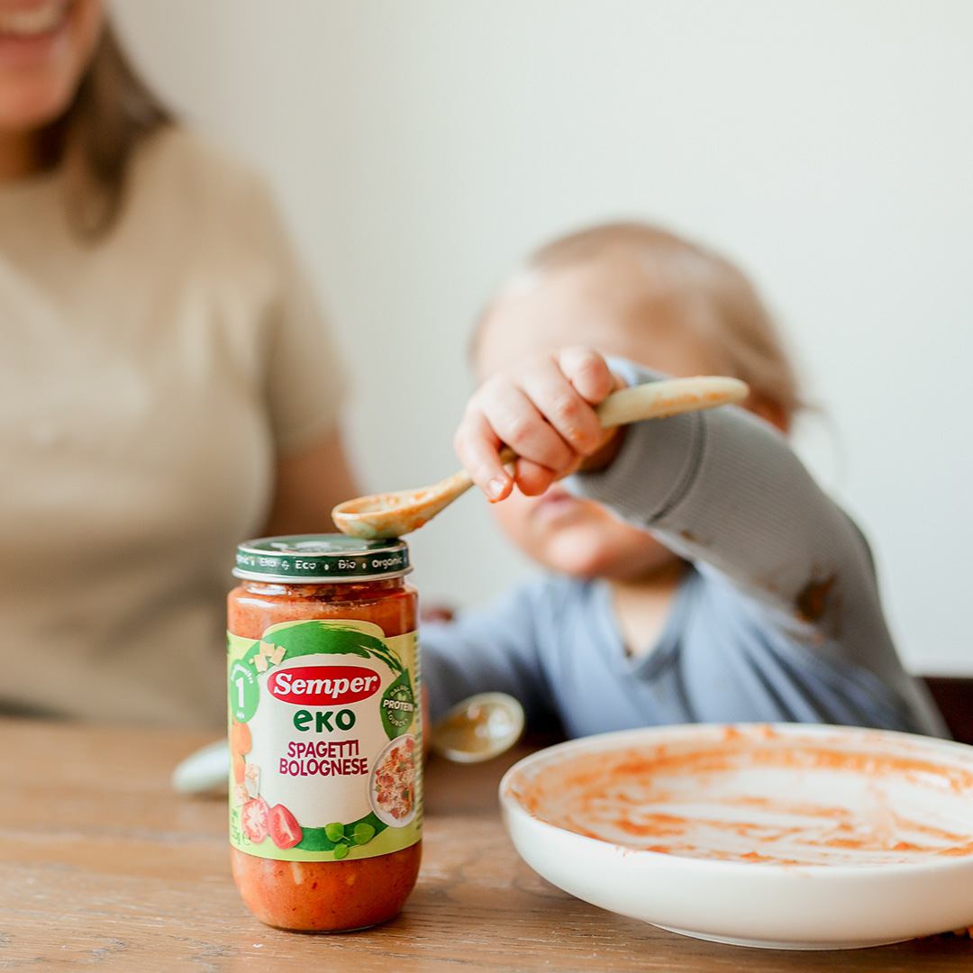 Baby touching Semper baby food jar with spoon